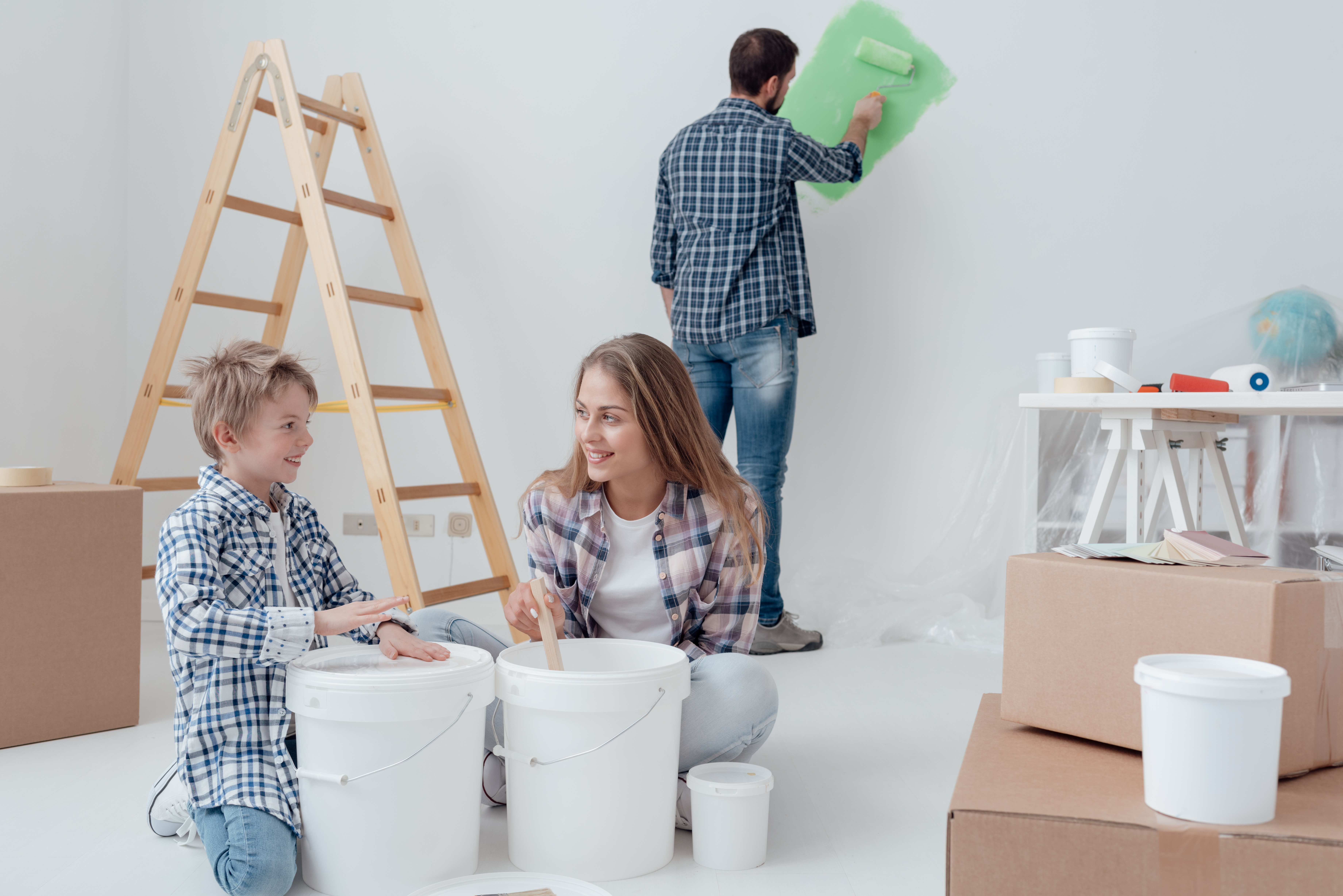 Young family doing a home makeover and painting rooms, the father is painting walls with a paint roller, the mother and her son are stirring paint in a bucket